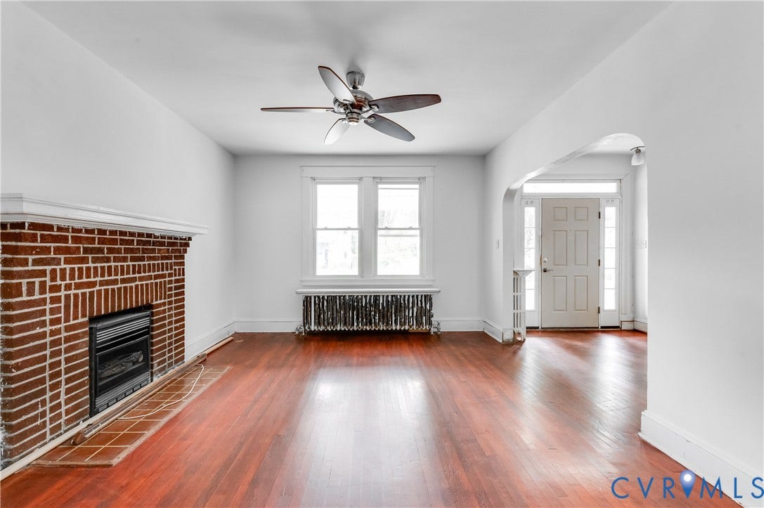 Hardwood flooring throughout, brick fireplace with mantel, ceiling fan, white trim, and a paneled entry door with sidelights