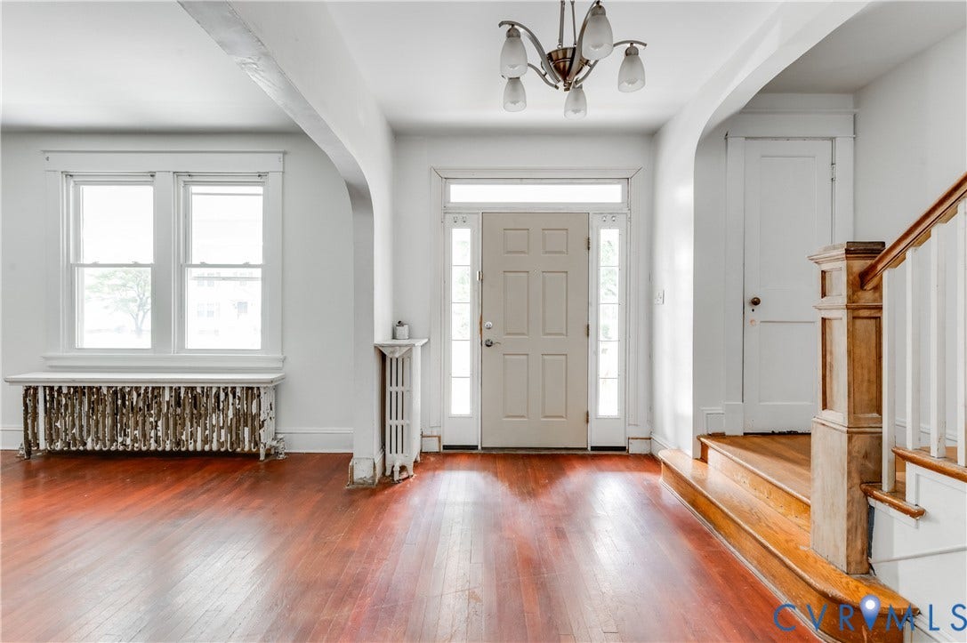 Hardwood flooring throughout, paneled entry door with sidelights, staircase with wood banister, chandelier lighting fixture, and arched entryway