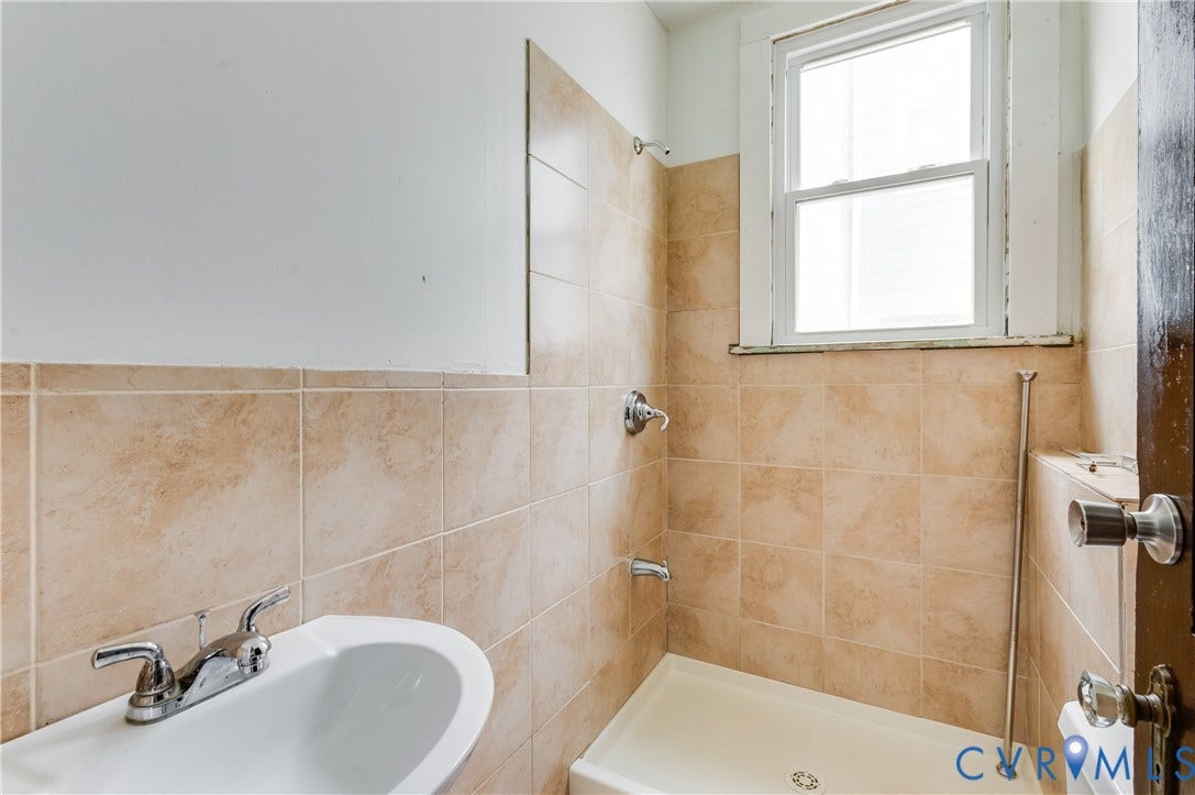 Pedestal sink with chrome faucet, tiled shower surround, integrated shower fixture, and a window
