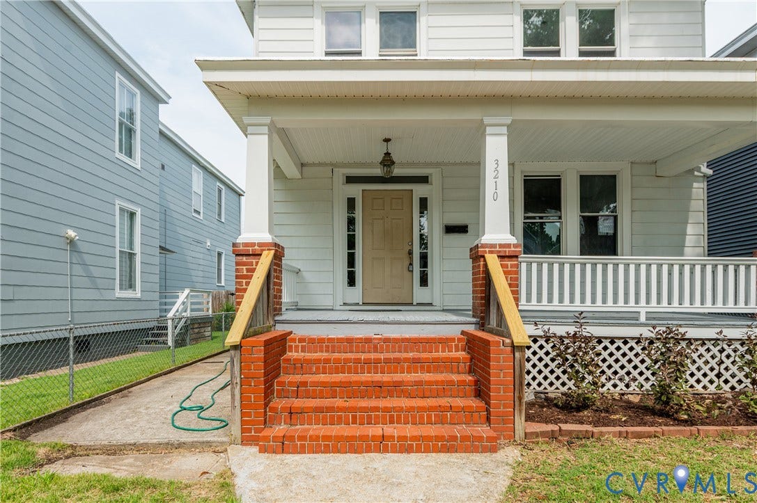 White exterior with a covered porch, brick steps, and an adjacent wood-paneled exterior