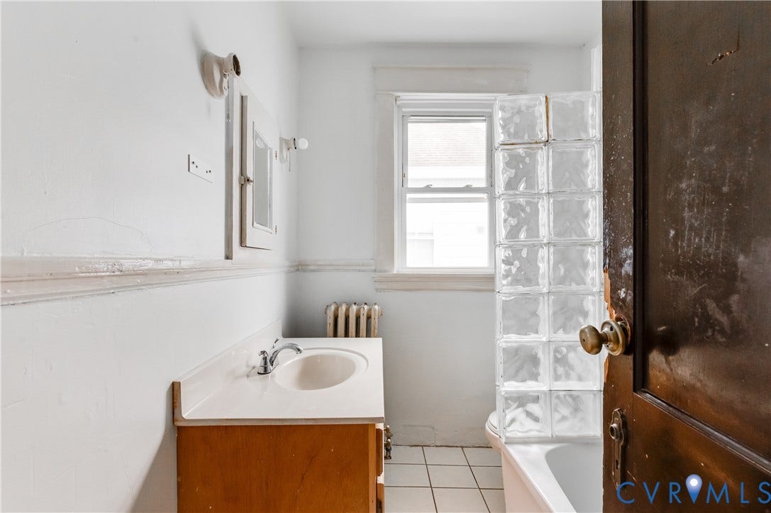 Wood-finish vanity with integrated sink, glass block shower partition, and white floor tiling