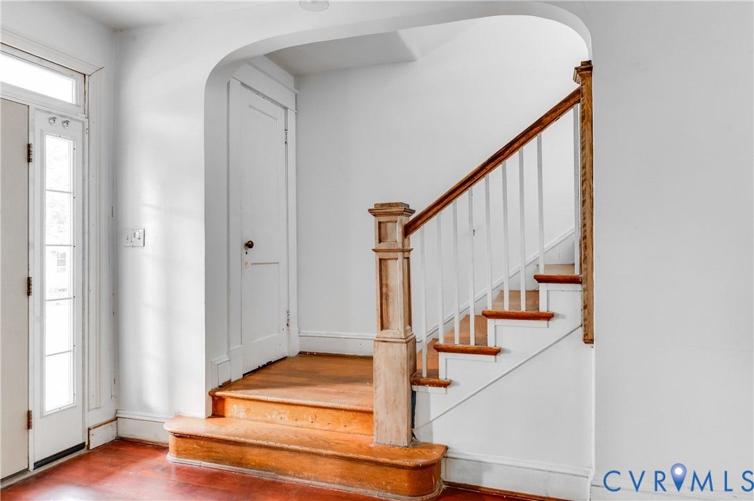 Archway entry leading to a wood-finish staircase with white risers and spindles, featuring a wood-finish handrail and newel post