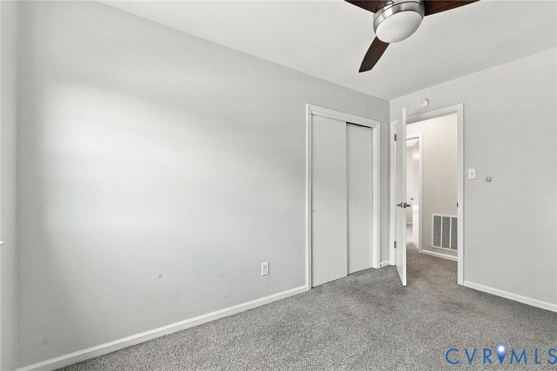 Grey wall-to-wall carpeting, white painted walls, and a ceiling fan with integrated lighting