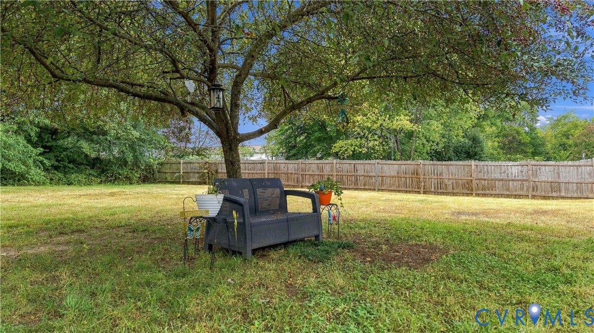 Expansive backyard featuring a mature tree, natural wood privacy fencing, and a clear sky backdrop