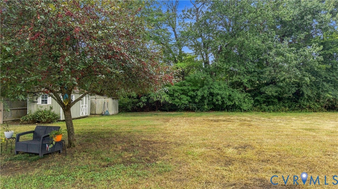 Expansive yard with mature trees, two storage sheds, and a partial privacy fence