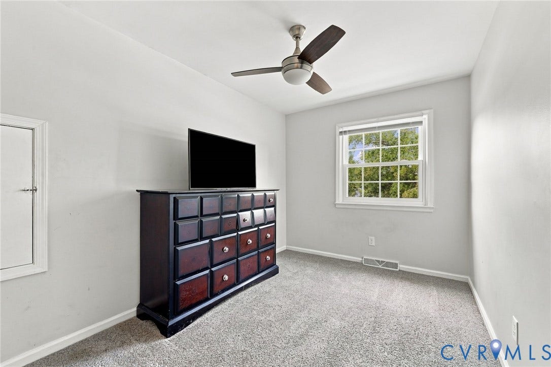 Neutral wall color, carpet flooring, window with natural light, and a ceiling fan with integrated lighting