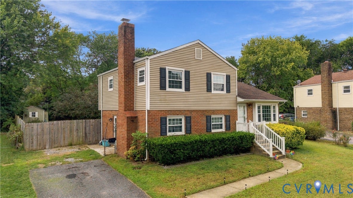 Two-story residence featuring brick and siding exterior, front entry porch, mature landscaping, and a fenced backyard with a storage shed