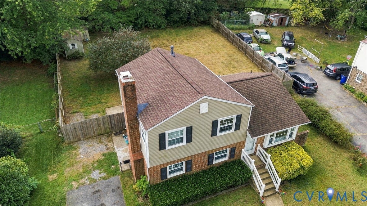 Split-level residence featuring a brick chimney, shingle roof, and a fenced backyard