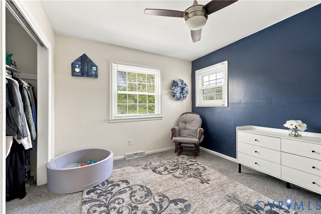 Neutrally painted walls with a contrasting accent wall, two windows, ceiling fan, and carpeted flooring