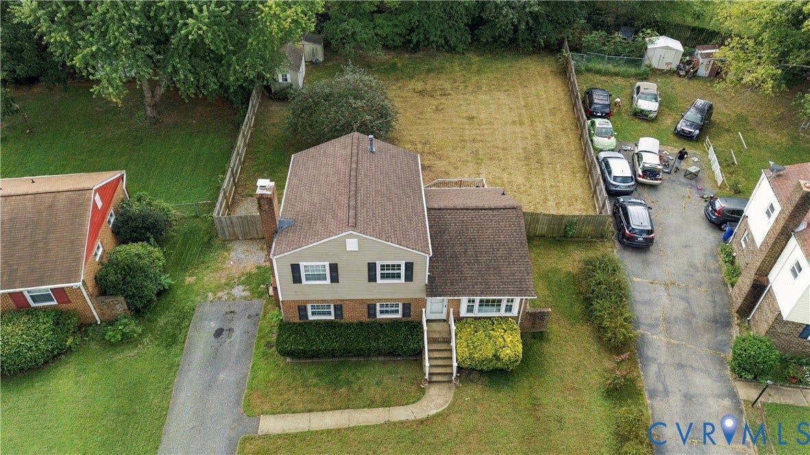 Two-story residence with a gabled roof and light-colored siding, featuring a front lawn with mature landscaping