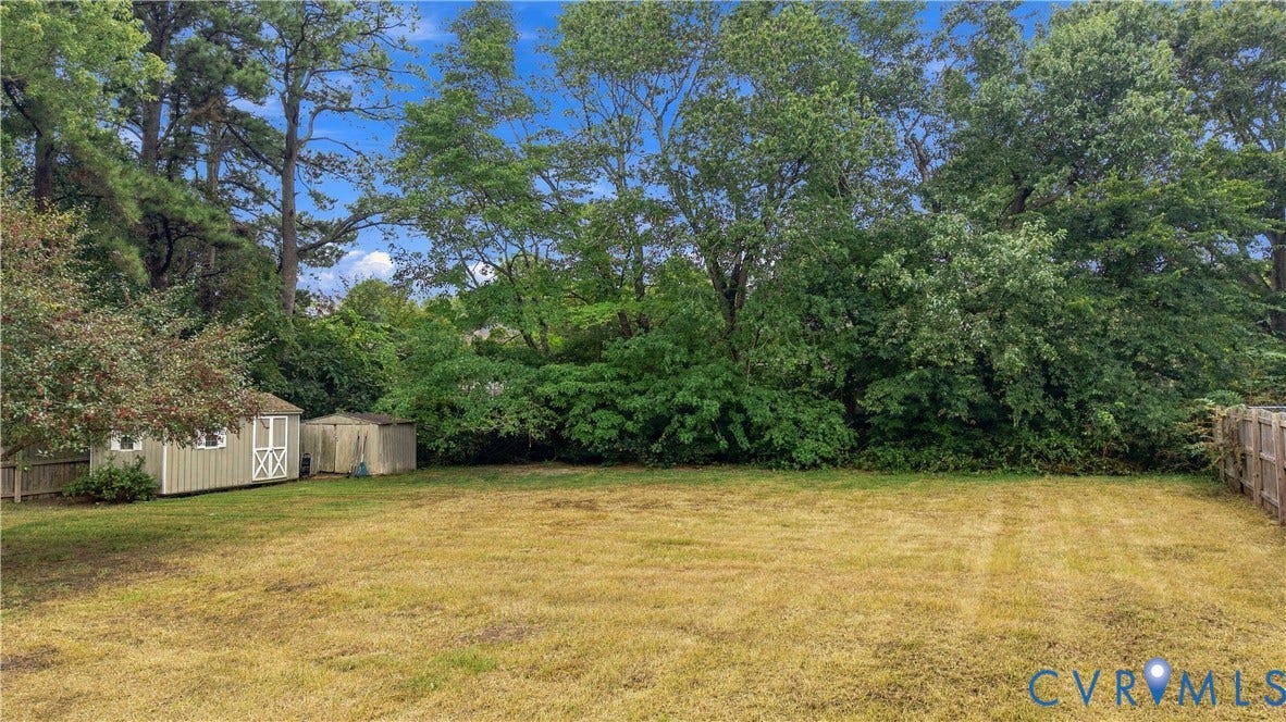 Expansive backyard featuring mature trees, a wooden privacy fence, and two storage sheds
