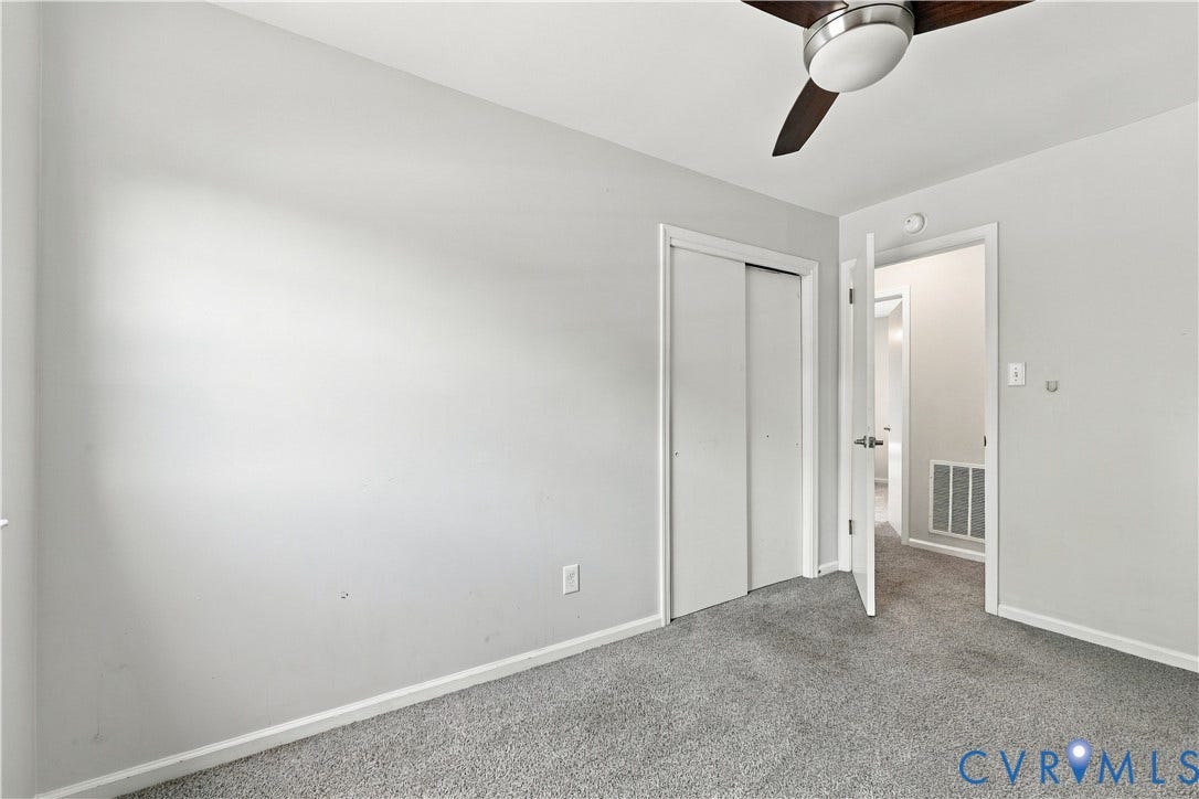 Neutral gray walls, plush gray carpet, ceiling fan with light fixture, and white bi-fold closet doors