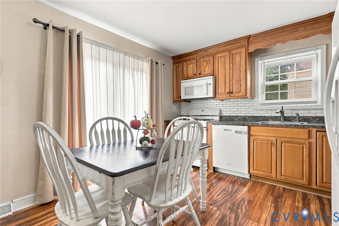 Wood-finish flooring, wood cabinetry, white subway tile backsplash, stainless steel sink, and a window with blinds