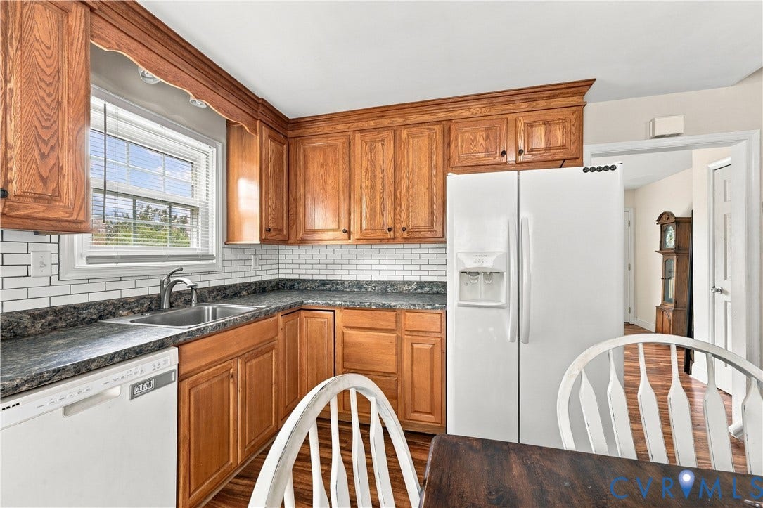 Kitchen featuring wood cabinetry, white subway tile backsplash, dark countertops, and a stainless steel sink with a white dishwasher