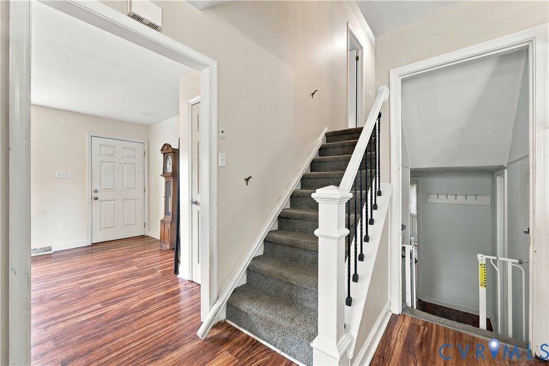 Wood-finish flooring, paneled entry door, carpeted staircase with white newel post and wrought iron balusters, and an entryway coat rack