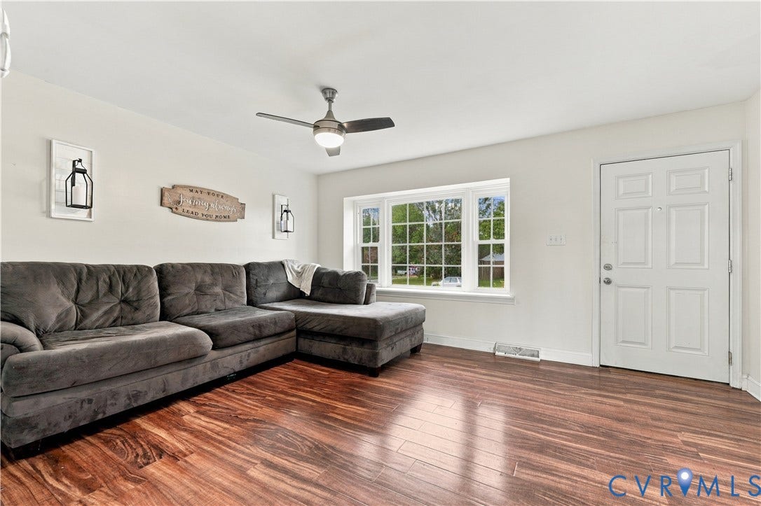 Wood-finish flooring, bay window, ceiling fan with integrated lighting, paneled entry door, and white painted walls
