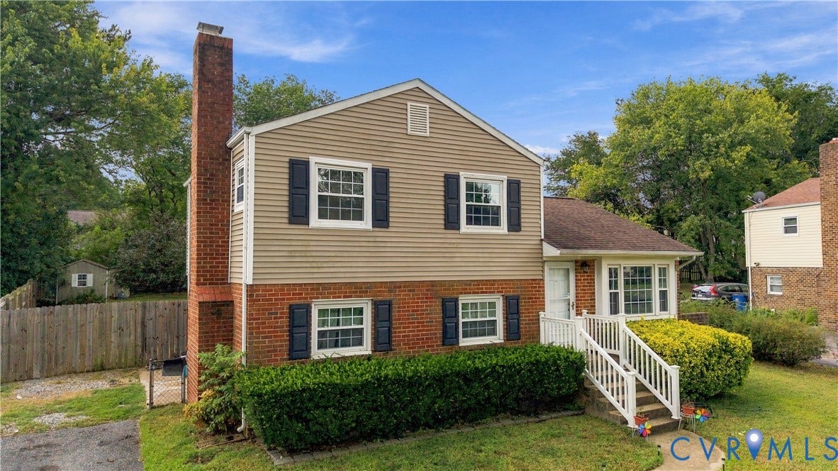 Two-story residence featuring brick and siding exterior, a prominent brick chimney, white window frames with dark shutters, and a front entry with white railings