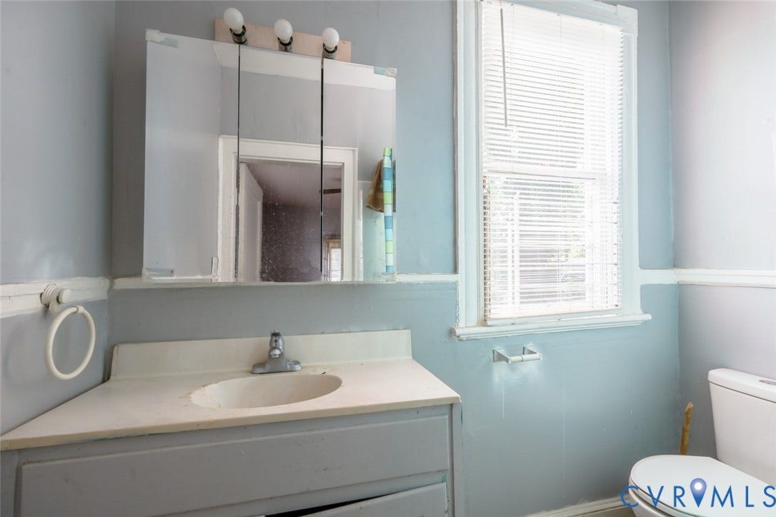 209 W 34th Street, Richmond, VA 23225 Bathroom featuring a single-sink vanity, wall-mounted mirror with integrated lighting, a window with blinds, and a toilet