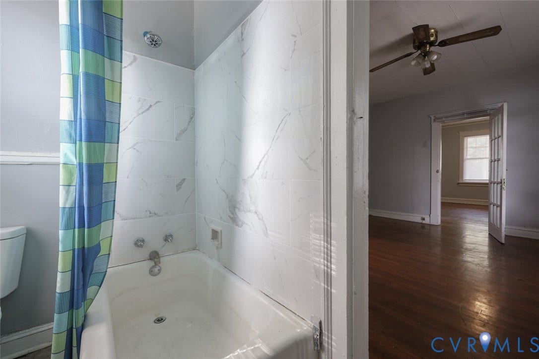 209 W 34th Street, Richmond, VA 23225 Bathtub with white tiled surround, chrome showerhead, and a white toilet