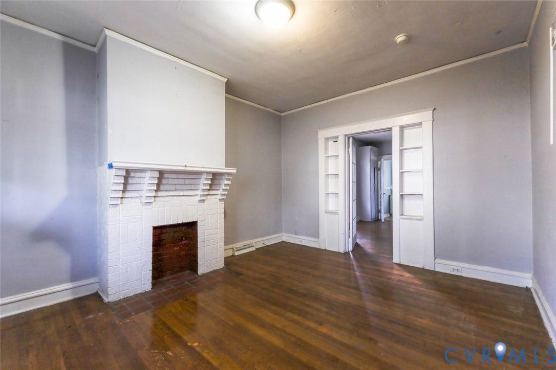 209 W 34th Street, Richmond, VA 23225 Wood-finish flooring, white brick fireplace with mantel, recessed built-in shelving, and light gray wall finish