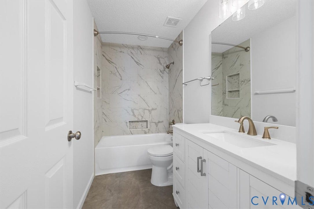 Bathroom featuring a tub/shower combination with marble-look tile surround and two recessed niches, a single vanity with a white countertop and stainless finish faucet, and a large wall-mounted mirror, new shower rod and bar towels holders