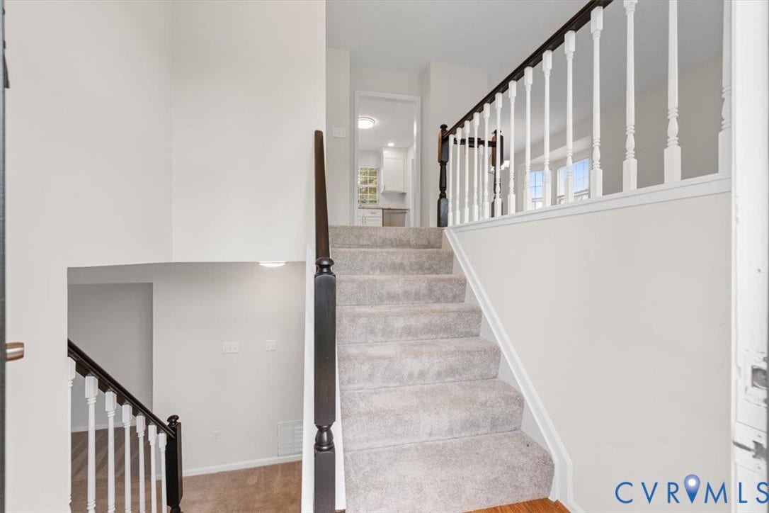 Carpeted staircase featuring a dark wood handrail and white balusters