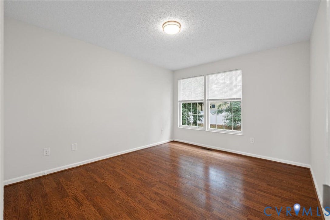 Hardwood flooring throughout, white walls, two windows, and a ceiling-mounted light fixture
