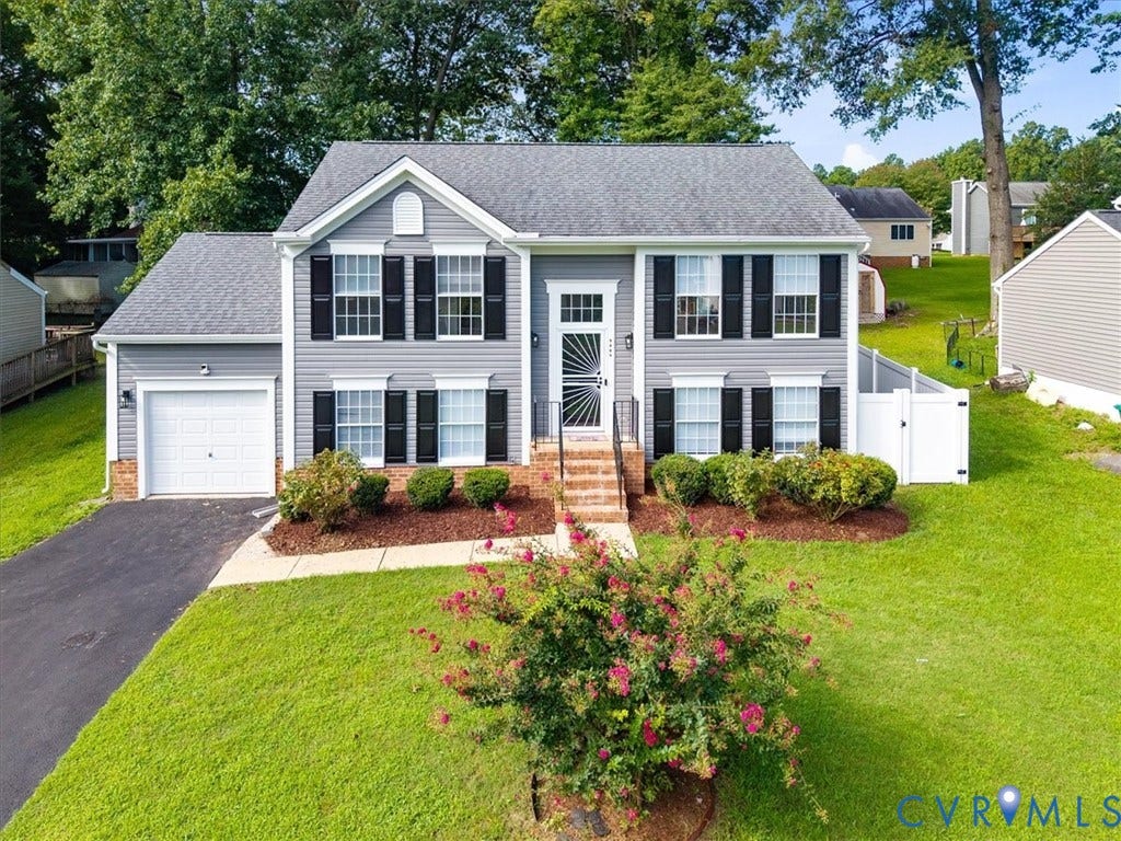 Gray siding exterior with a white garage door, black window shutters, and a front entry with a storm door
