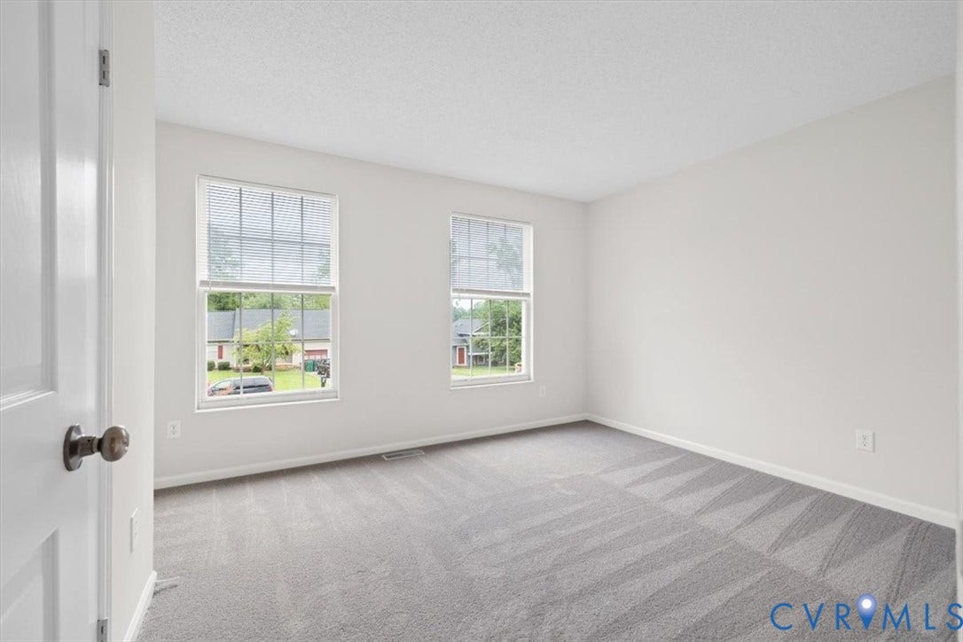 Light gray wall paint, textured ceiling, gray carpet flooring, two windows with blinds, white trim