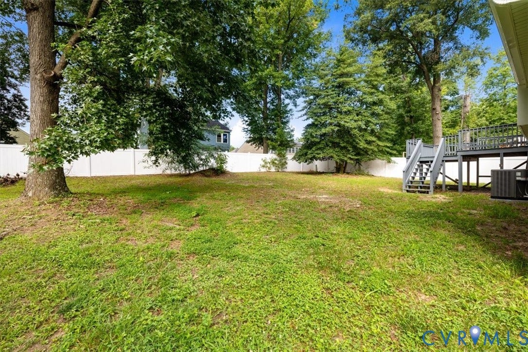 Spacious yard featuring a large tree, perimeter fencing, and a multi-level deck with stairs