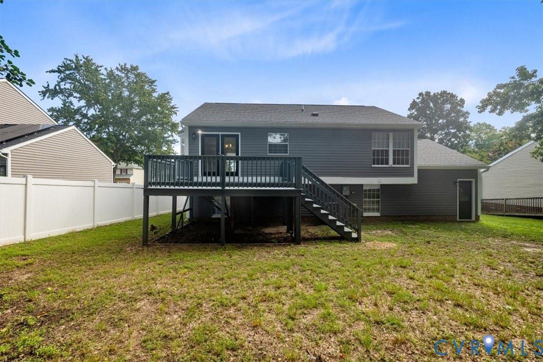 Spacious rear deck with black railings and staircase offering outdoor entertaining space, overlooking a large, level lawn surrounded by mature trees and neighboring properties