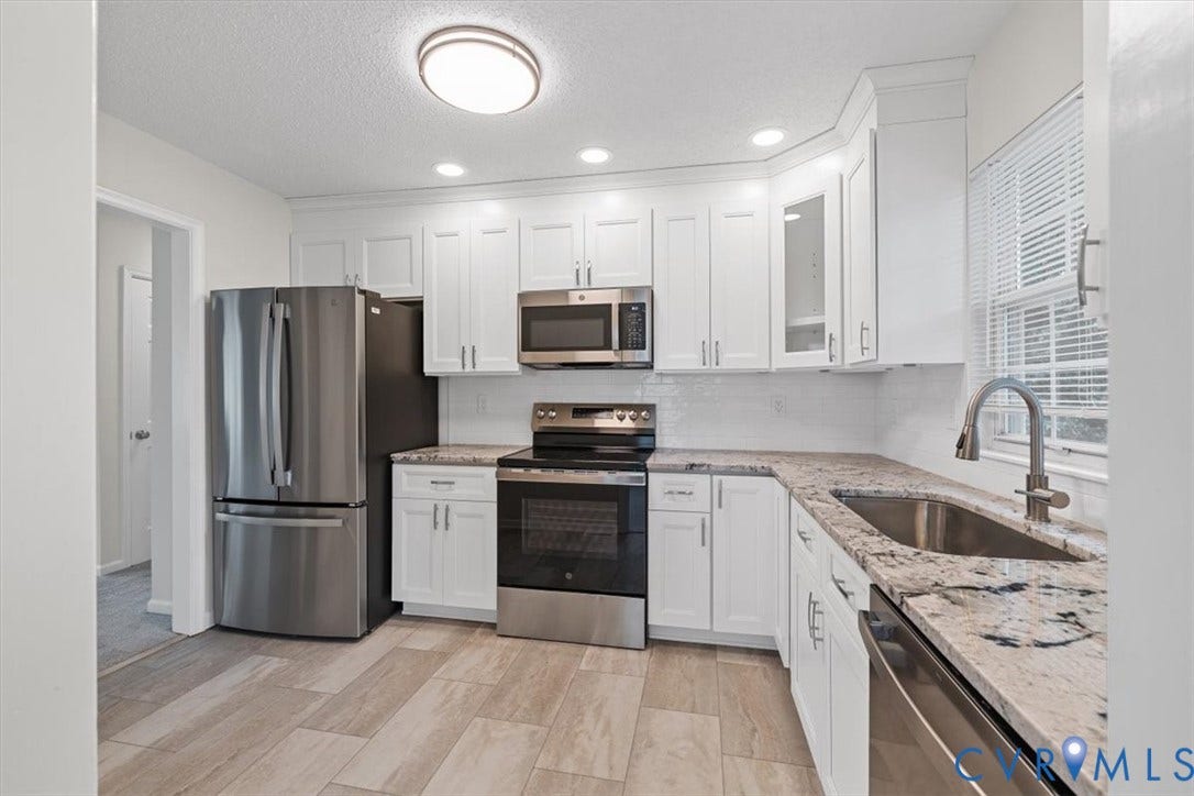 Kitchen featuring white cabinetry, stainless steel appliances, speckled countertops, a subway tile backsplash, and light-toned tile flooring