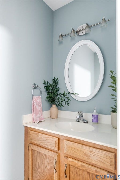 2844 Broadford Lane, Henrico, VA 23233 Vanity with a white countertop and integrated sink, wood-finish cabinetry, an oval framed mirror, and a three-light track fixture