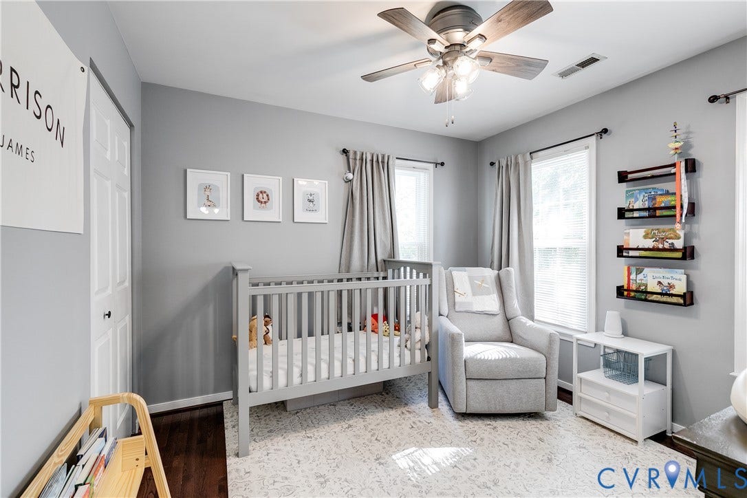 2844 Broadford Lane, Henrico, VA 23233 Bright nursery featuring dual windows with natural light, soft gray walls, ceiling fan with integrated lighting, white crib, upholstered glider chair, white storage unit with open shelving, and light-toned area rug
