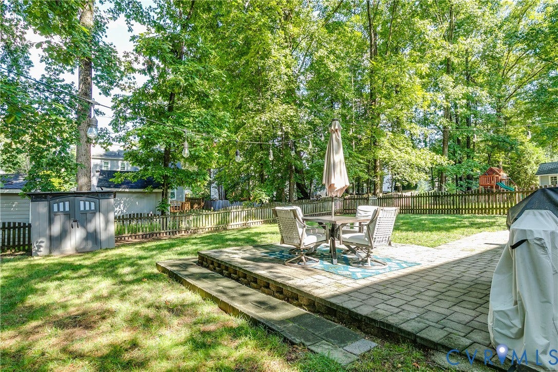 2844 Broadford Lane, Henrico, VA 23233 Expansive backyard featuring a stone paver patio, wood picket fencing, mature trees, and an outdoor storage shed