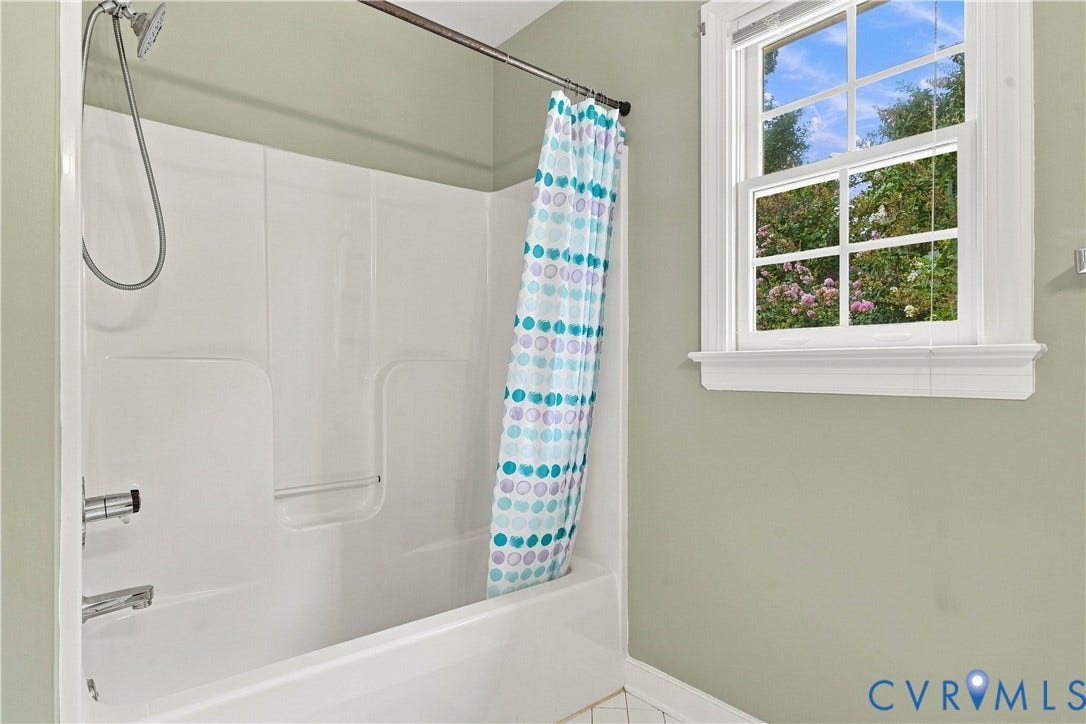 Tub/shower combination with a white surround, chrome fixtures, and a multi-pane window