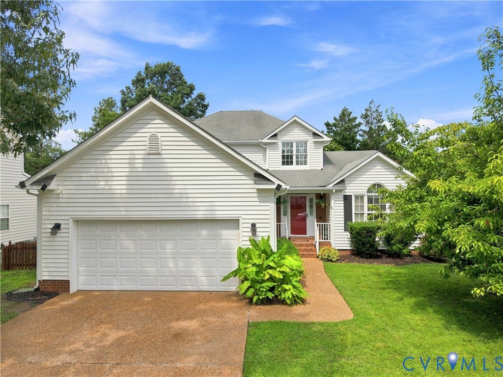 exterior entry door, attached two-car garage, dormer window, and mature landscaping
