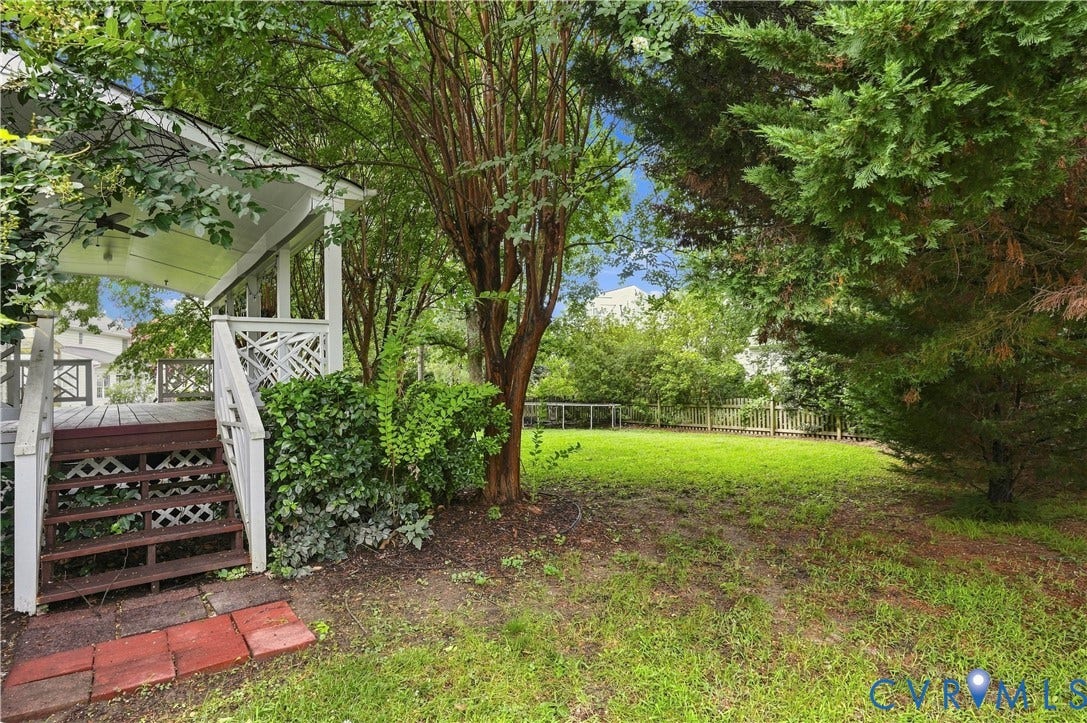 Expansive outdoor area with a wooden deck, lattice railings, mature trees, and a grassy lawn