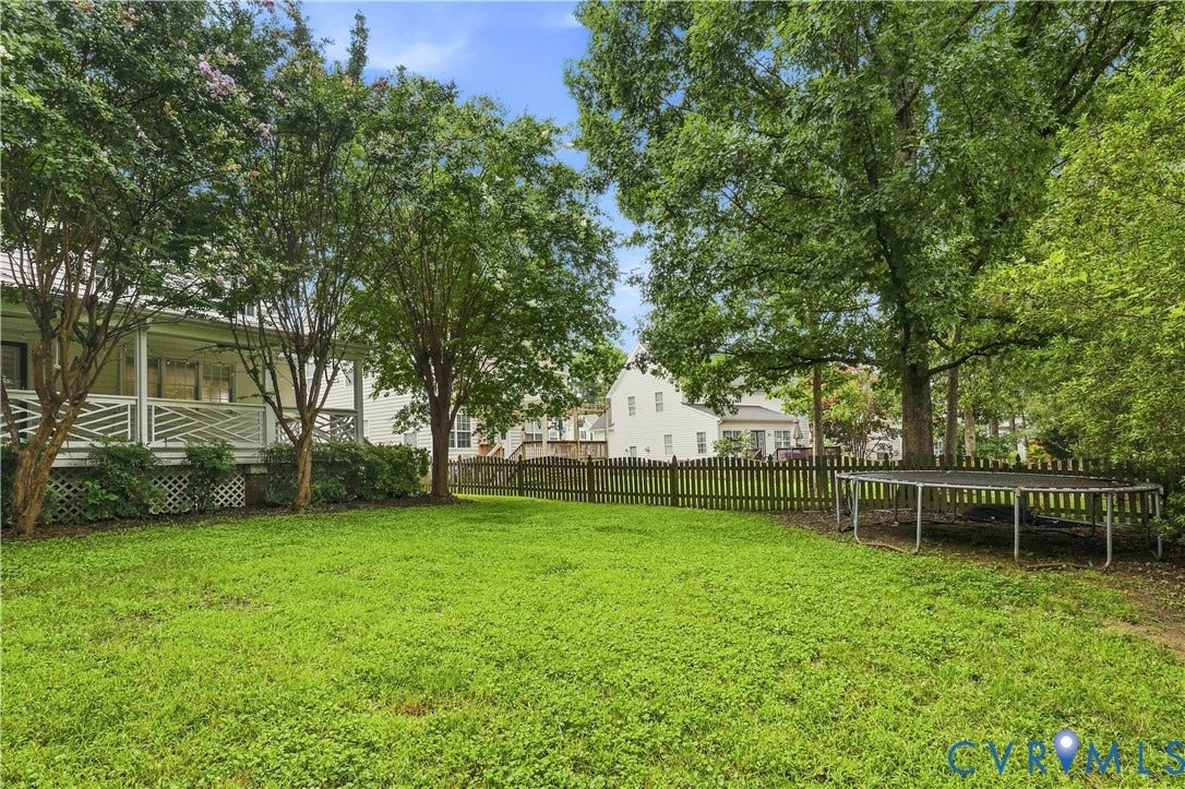 Expansive green lawn with mature trees, fenced perimeter, and a covered porch with white railing