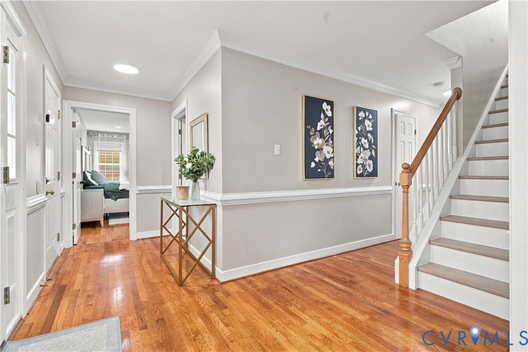 Wood-finish flooring throughout the hallway, wainscoting details, crown molding, and a staircase with a wood handrail