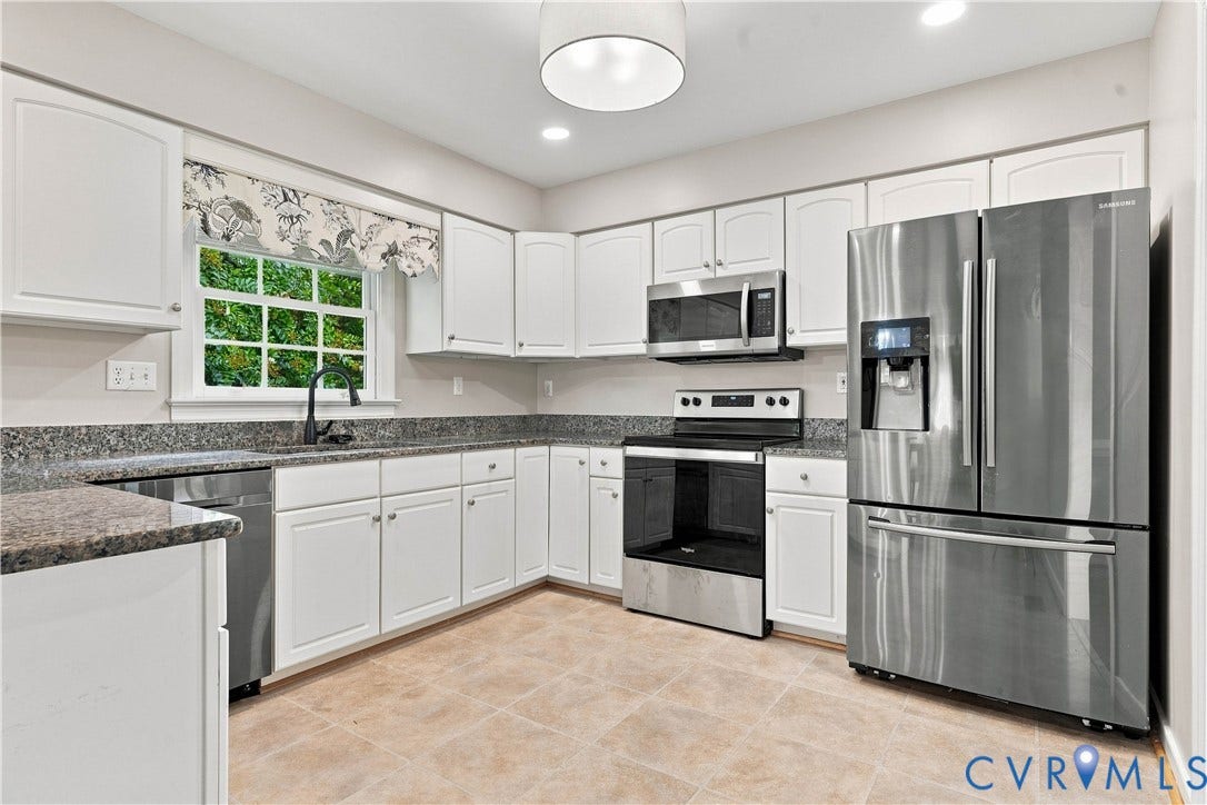 Kitchen featuring white cabinetry, dark speckled countertops, stainless steel appliances, and neutral-toned floor tiling