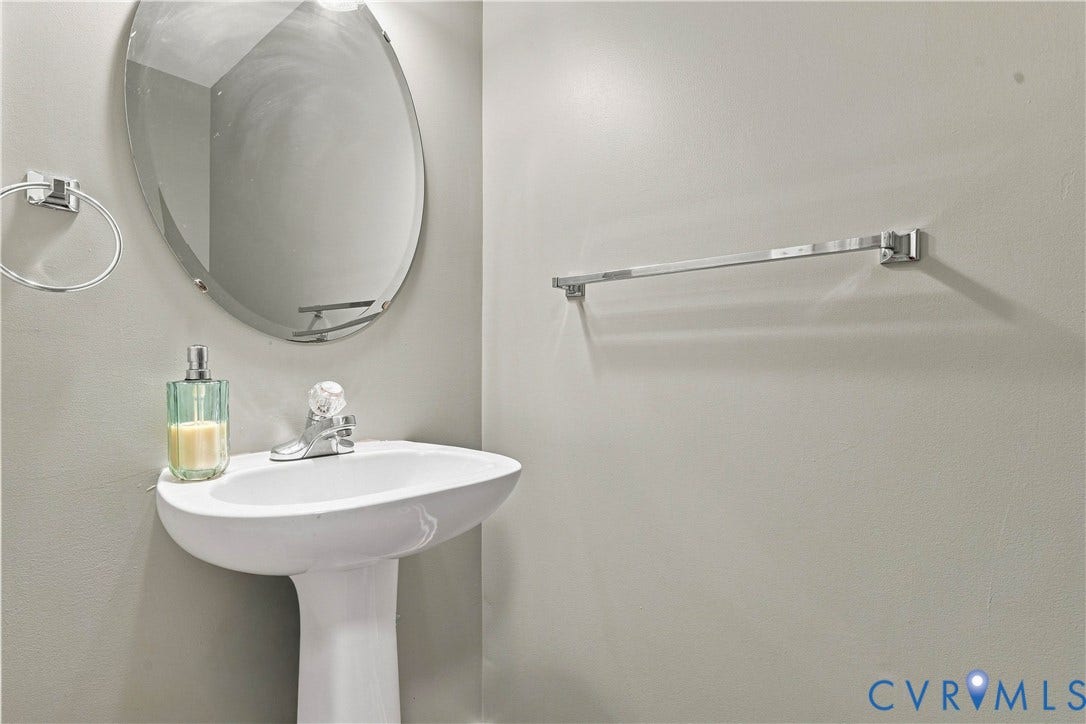 Half Bath Pedestal sink with a polished chrome faucet, an oval wall-mounted mirror, and a chrome towel bar