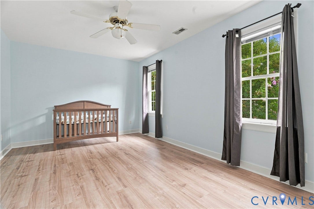 Wood-finish flooring with light-toned walls, featuring two windows with dark curtain rods