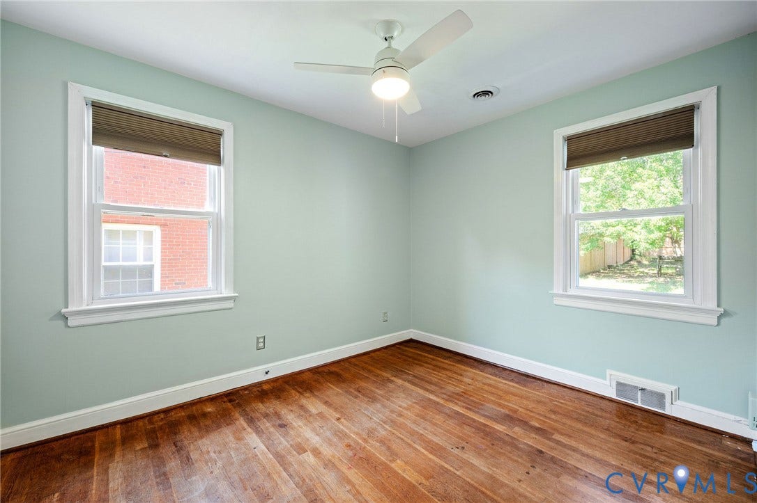 808 W 47th Street, Richmond, VA 23225 Hardwood flooring, two windows with white trim, ceiling fan with integrated lighting, and light-colored wall paint