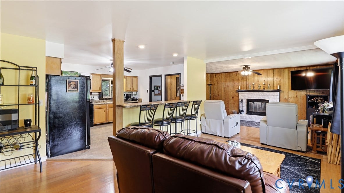 11201 Monday Way, Chesterfield, VA 23112 Open-concept living space featuring wood-finish flooring, a kitchen with light wood cabinetry, a breakfast bar, a fireplace with a white brick surround, and wood paneling