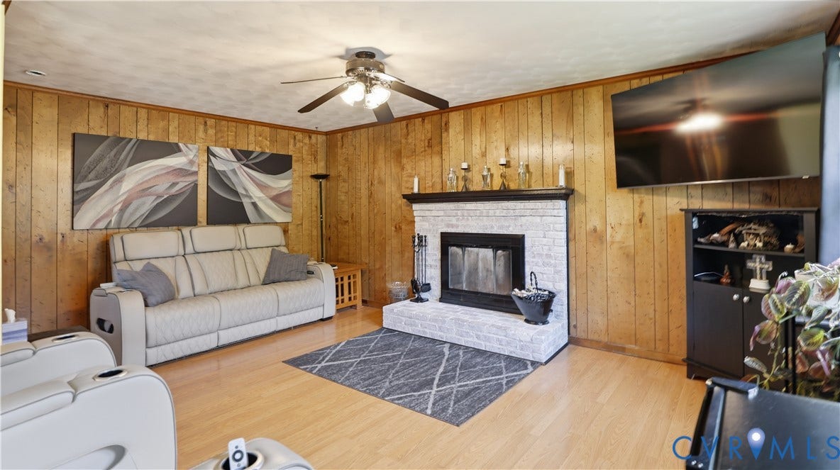 11201 Monday Way, Chesterfield, VA 23112 Wood-paneled walls, light wood-finish flooring, white brick fireplace with a black mantel, and a ceiling fan with integrated lighting