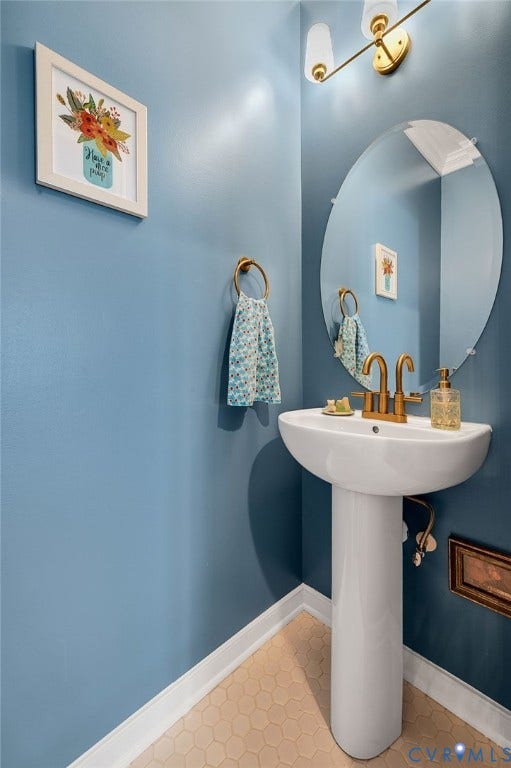 2811 Murano Way, The Villas At Hunton Park, Glen Allen, VA 23059 Powder room featuring a pedestal sink with brass fixtures, oversized circular mirror with integrated lighting, and soft blue walls with darker blue lower paneling