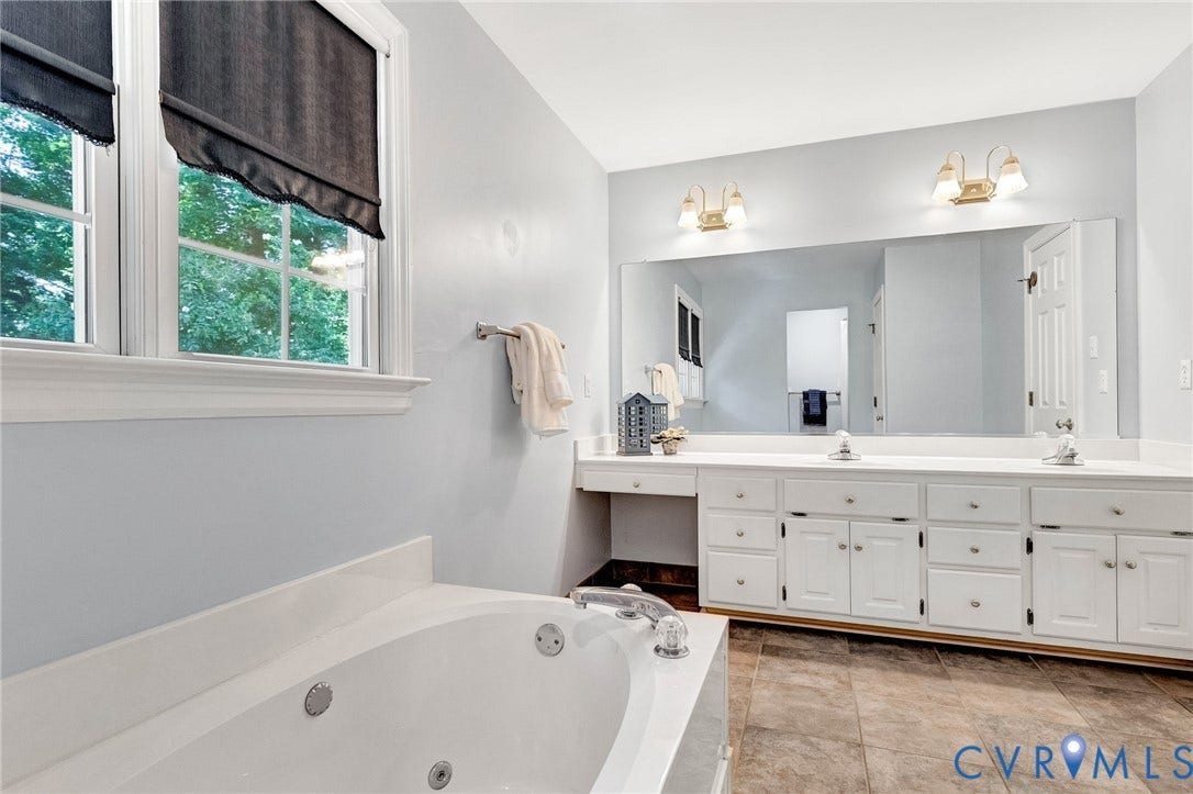 16406 Inchcape Road, Chesterfield, VA 23120 Soaking tub with integrated jets, dual vanity with white cabinetry, light-toned countertops, and expansive wall mirror