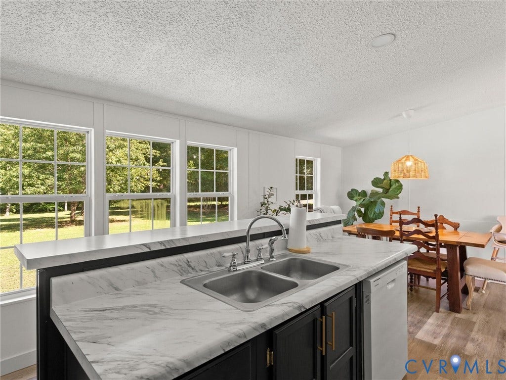 4554 Powhatan Lakes Road, Powhatan, VA 23139 Chef's kitchen anchored by a striking black island with marble-finish countertops and an undermount sink, complemented by stainless steel faucetry and abundant natural light from oversized multi-pane windows