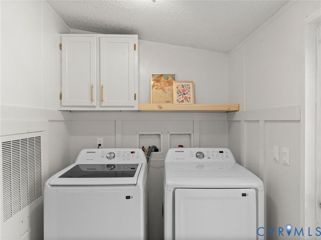 4554 Powhatan Lakes Road, Powhatan, VA 23139 Dedicated laundry room featuring side-by-side washer and dryer, white cabinetry with brass hardware, wooden floating shelf for storage and display, and neutral walls with wainscoting detail